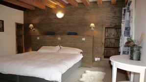 Een slaapkamer met een bed, een houten hoofdbord, twee wandlampen, een klein wit tafeltje en een zacht, wit vloerkleed.