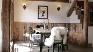 Een eetruimte met houten wanden, een houten tafel en stoelen. Er hangt een poster aan de muur en op de tafel staat een kandelaar.