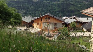 Een houten chalet met een schuin dak, omgeven door weelderige begroeiing en bergen op de achtergrond.