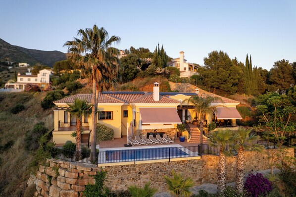 A Mediterranean-style villa with a stone retaining wall, a swimming pool, and a view of the surrounding hills. - Ultra-Luxury Villa with Private Pool, Art Deco Cinema & 1950s Diner– Sleeps 6 (Mijas)