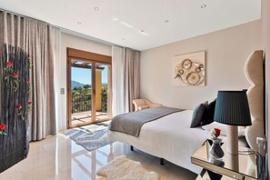 Ein modernes Schlafzimmer mit Bett, Nachttisch, Lampe, einer Vase mit einer Blume und Blick ins Freie.
