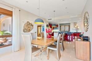 Een moderne eetruimte met een tafel met glazen blad, tijdloze stoelen en hanglampen.