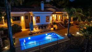 Vue d’une maison avec piscine, des chaises longues et un escalier menant à l’étage supérieur, le tout vu depuis le bord de la piscine.