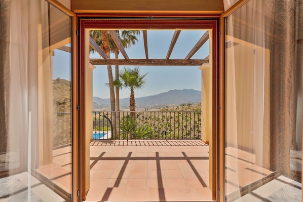 A balcony with a view of mountains, a pool, and palm trees. - Ultra-Luxury Villa with Private Pool, Art Deco Cinema & 1950s Diner– Sleeps 6 (Mijas)