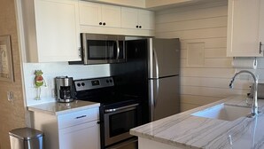 A modern kitchen with white cabinets, stainless steel appliances, a marble countertop, and a built-in oven. - Affordable Paradise  (Kihei)