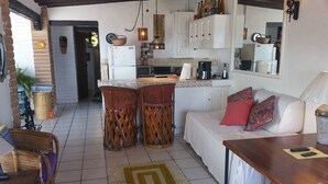 A compact kitchen with white cabinets, a microwave, and a coffee maker. There is a dining area with a sofa and a table. - Heart Of Town,  Ocean Views, Pool, Walking Distance To Beach (Puerto Vallarata)