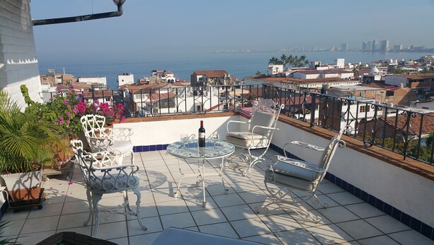 A terrace with outdoor furniture, a view of the sea, and buildings in the background. - Heart Of Town,  Ocean Views, Pool, Walking Distance To Beach (Puerto Vallarata)