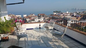 Eine Terrasse mit Gartenmöbeln, Blick aufs Meer und Gebäuden im Hintergrund.