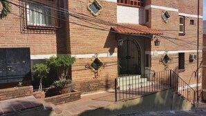 A traditional brick building with a tiled roof, a gated entrance, and a small garden area with potted plants. - Heart Of Town,  Ocean Views, Pool, Walking Distance To Beach (Puerto Vallarata)