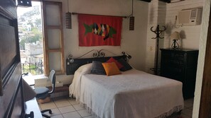 Ein Schlafzimmer mit einem Bett, einem Sessel, einem Schreibtisch, einem Fenster und einem Wandheizgerät.