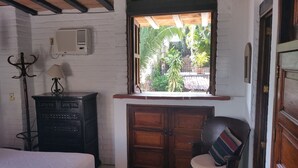 A room with a bed, a desk with a lamp, a wooden cabinet, and a window with a view of greenery. - Heart Of Town,  Ocean Views, Pool, Walking Distance To Beach (Puerto Vallarata)