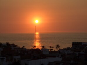 Ein Sonnenuntergang über dem Meer mit Gebäuden im Vordergrund.
