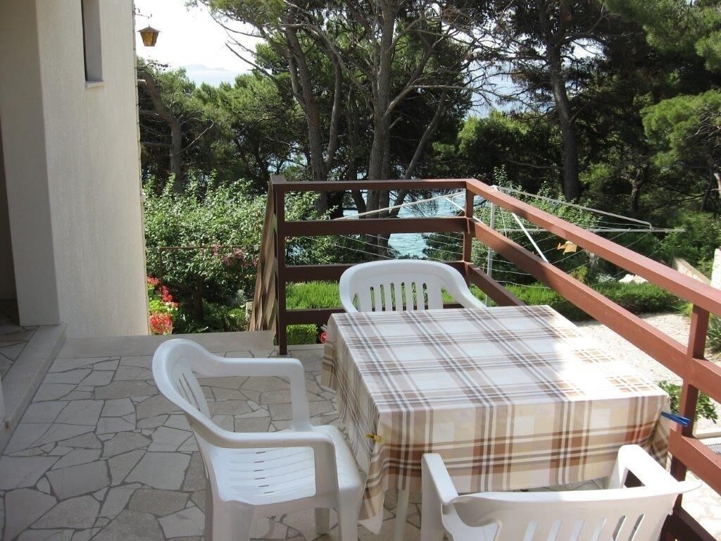 Un patio con mesa y sillas, baranda de madera y vistas a árboles y follaje.