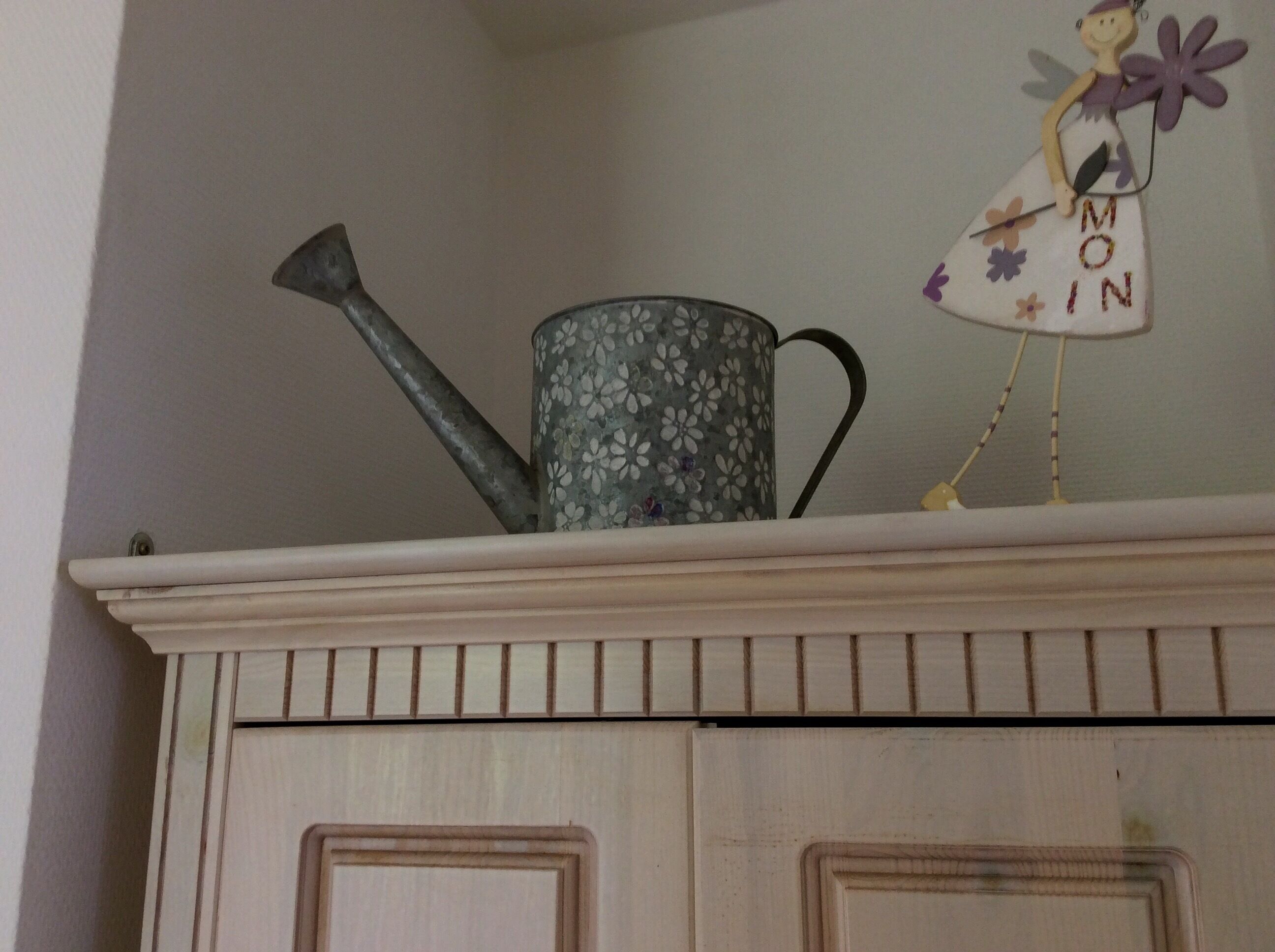 A floral-patterned watering can on a shelf above a wooden cabinet.