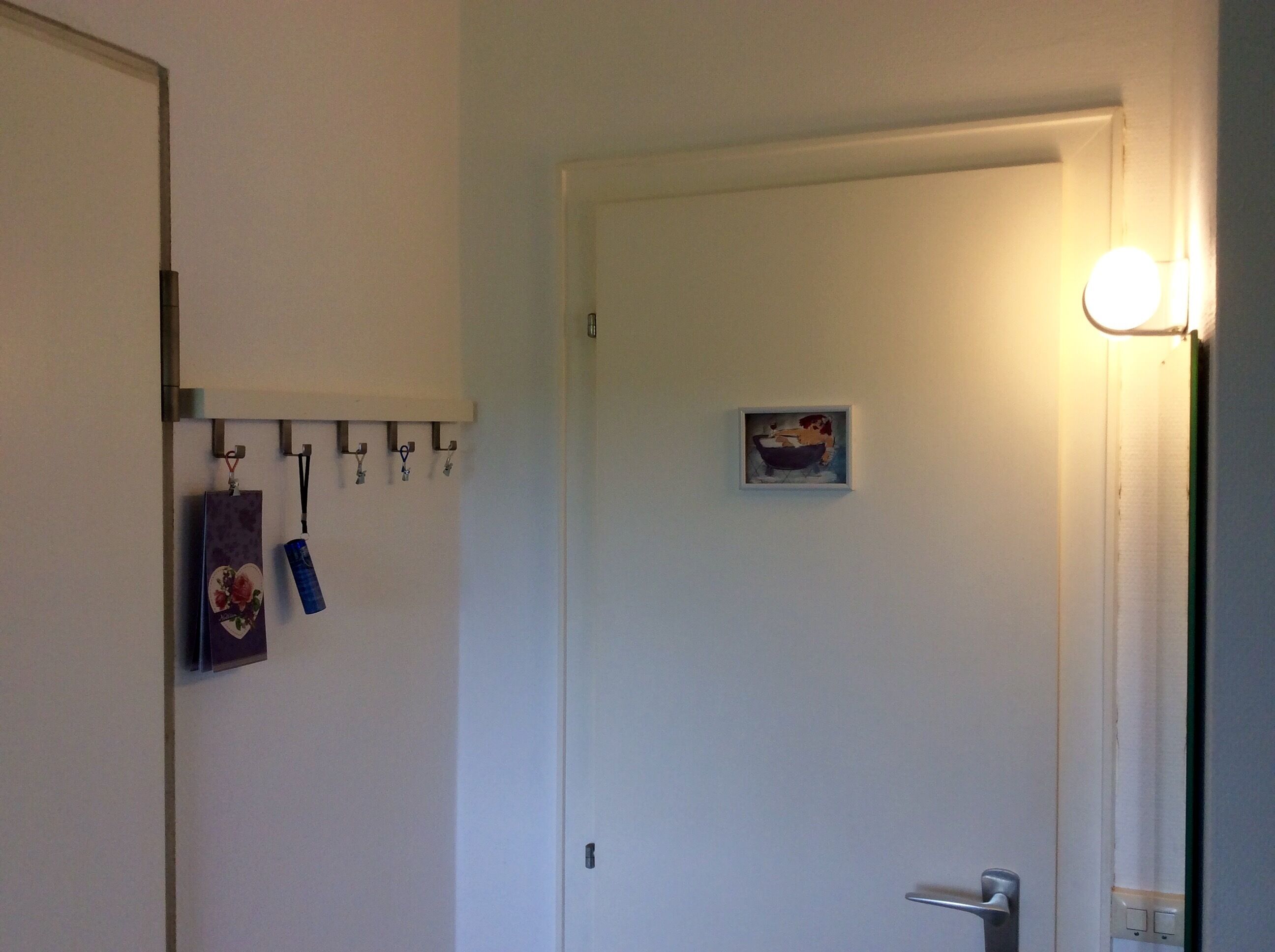 A room with a white door, a small framed picture on the wall, and a light fixture above the door.