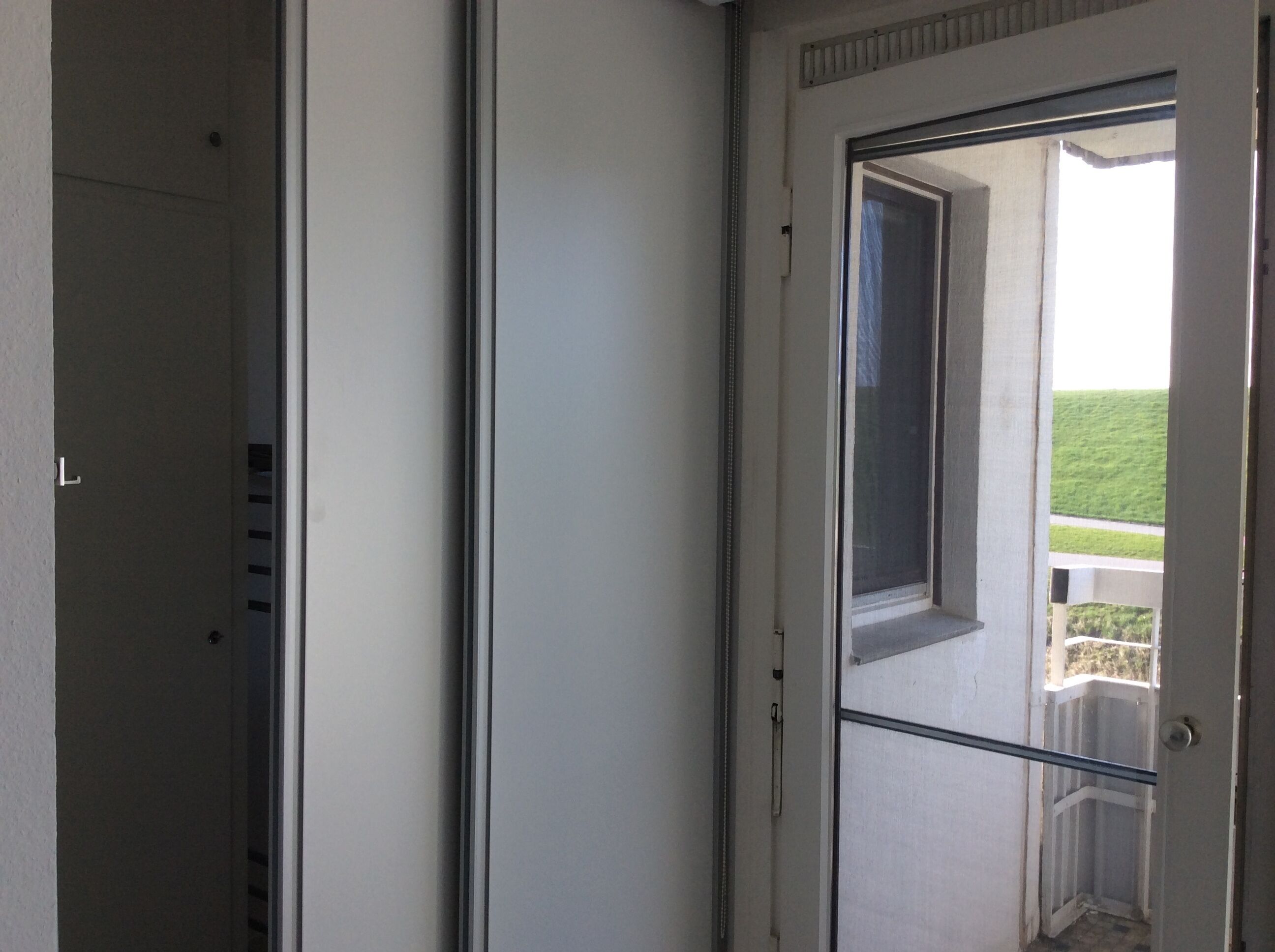 A room with a sliding door leading to a balcony with a view of a green landscape.