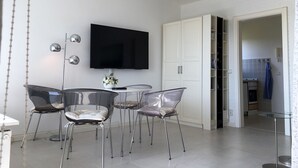 Een moderne keuken met een flatscreen televisie, witte kasten en een eethoek met transparante stoelen.