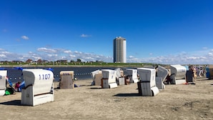 Accommodatie aan het strand met genummerde tenten, een rivier en een hoog gebouw op de achtergrond.