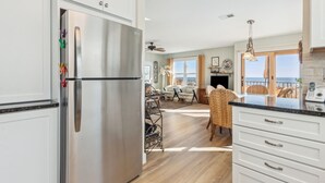 A modern kitchen with a stainless steel refrigerator, white cabinetry, and a dining area with wicker chairs.