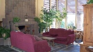 A cozy living room with a fireplace, two red sofas, and a coffee table. There are several potted plants and a wooden cabinet. - Rare Ventana Canyon Intimacy,  Heated Pools, Tennis (Tucson)