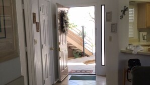 A hallway with a tiled floor leading to a door with a wreath, a staircase, and a view of a garden. - Rare Ventana Canyon Intimacy,  Heated Pools, Tennis (Tucson)