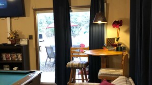 Una sala de estar acogedora con mesa de billar, sofá con cojines, mesa de comedor con sillas y televisor montado en la pared.