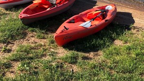 Tres kayaks rojos alineados en la orilla de un río tranquilo, bordeada de hierba.