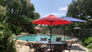 Un patio trasero con piscina, terraza de piedra y mobiliario exterior.