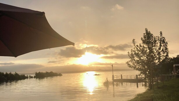 Vista de un atardecer desde un patio junto al lago con sillas y una mesa.
