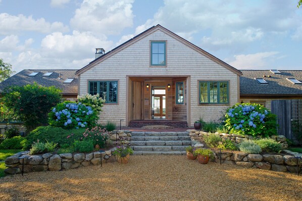 A two-story house with a prominent front entrance, a stone staircase, and a well-maintained garden with hydrangeas. - Light Open Vacation Home, Sweeping Waterviews, Hill Top, Private  (Chilmark)