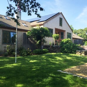 A two-story house with a sloped roof, a stone foundation, and a well-maintained lawn. - Light Open Vacation Home, Sweeping Waterviews, Hill Top, Private  (Chilmark)