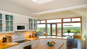 Een moderne keuken met witte kasten, een houten aanrechtblad en een groot raam met uitzicht op groen.