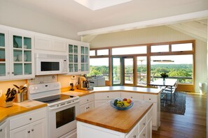 A modern kitchen with white cabinetry, a wooden countertop, and a large window offering a view of greenery. - Light Open Vacation Home, Sweeping Waterviews, Hill Top, Private  (Chilmark)