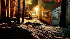 Eine Hütte mit einer Treppe, die zu einer Veranda führt, umgeben von Bäumen und verschneitem Gelände.