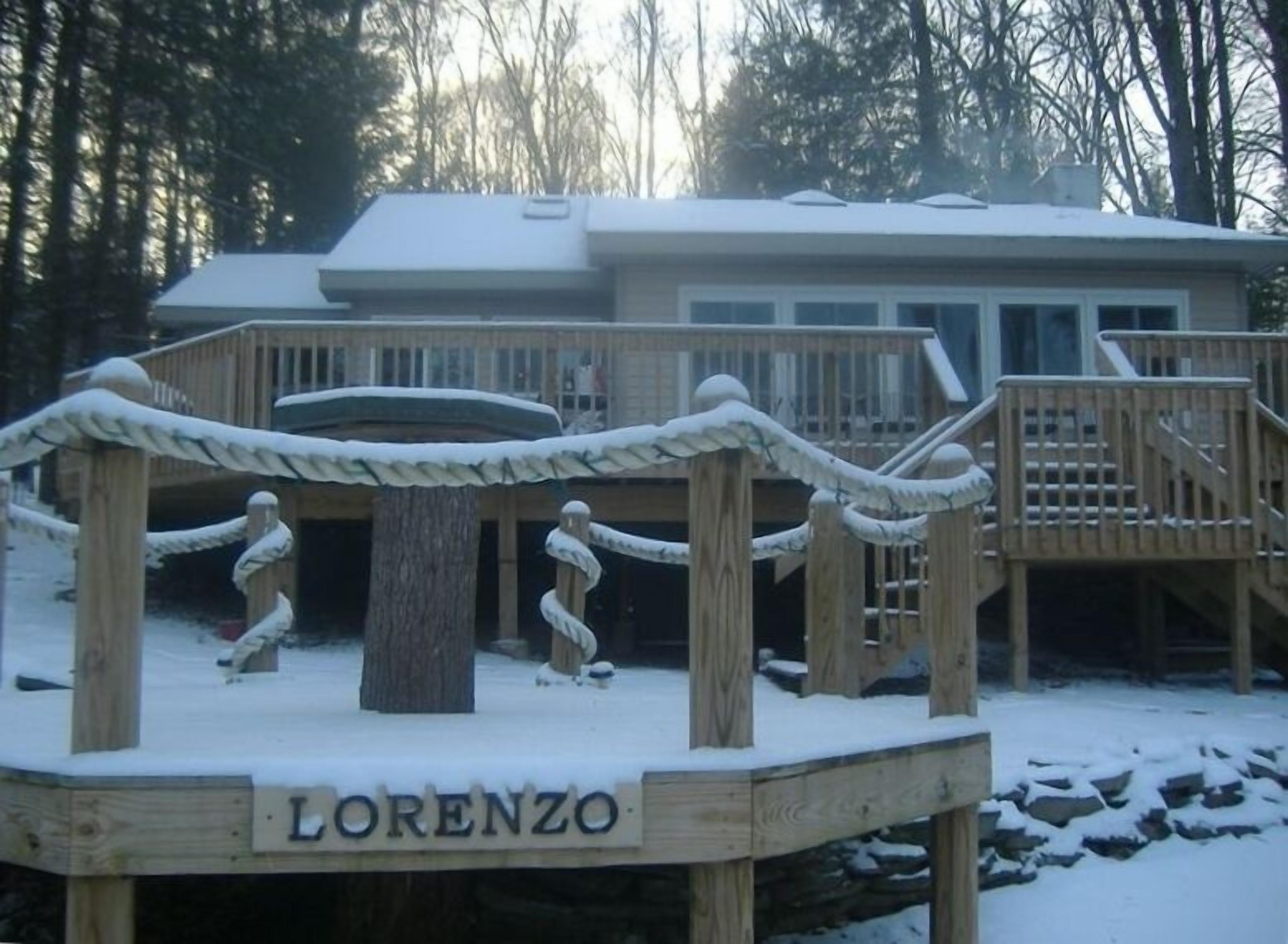 A wooden deck with a name sign reading "Lorenzo," surrounded by snow and trees.