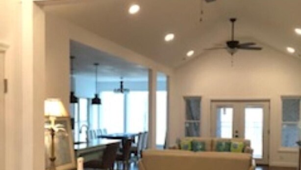 A spacious living room with a high ceiling and a ceiling fan, a dining area with a table and chairs, and a sofa with cushions.