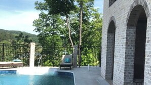 A swimming pool with a metal ladder, surrounded by a brick building with arched windows and a fence.