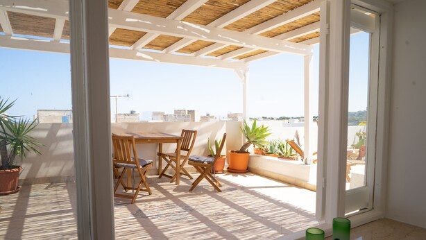 En solbeskinnet terrasse med et bord og stole, potteplanter og udsigt over bybilledet.