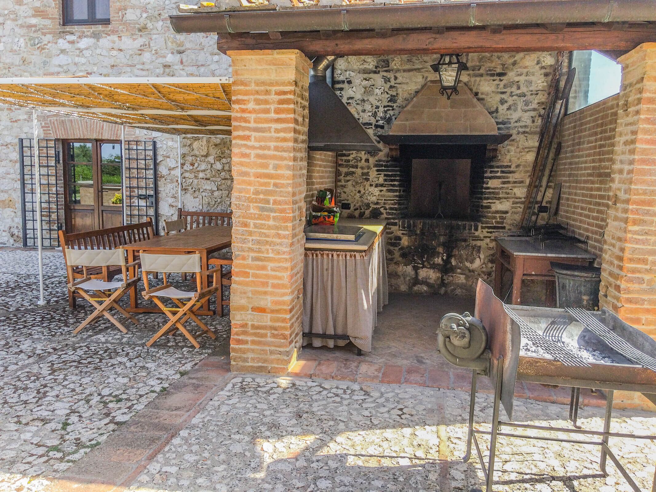 An outdoor patio area with a brick oven, wooden furniture, and a stone wall.