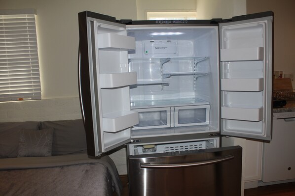 An open refrigerator with multiple shelves and compartments, a microwave, and a freezer.