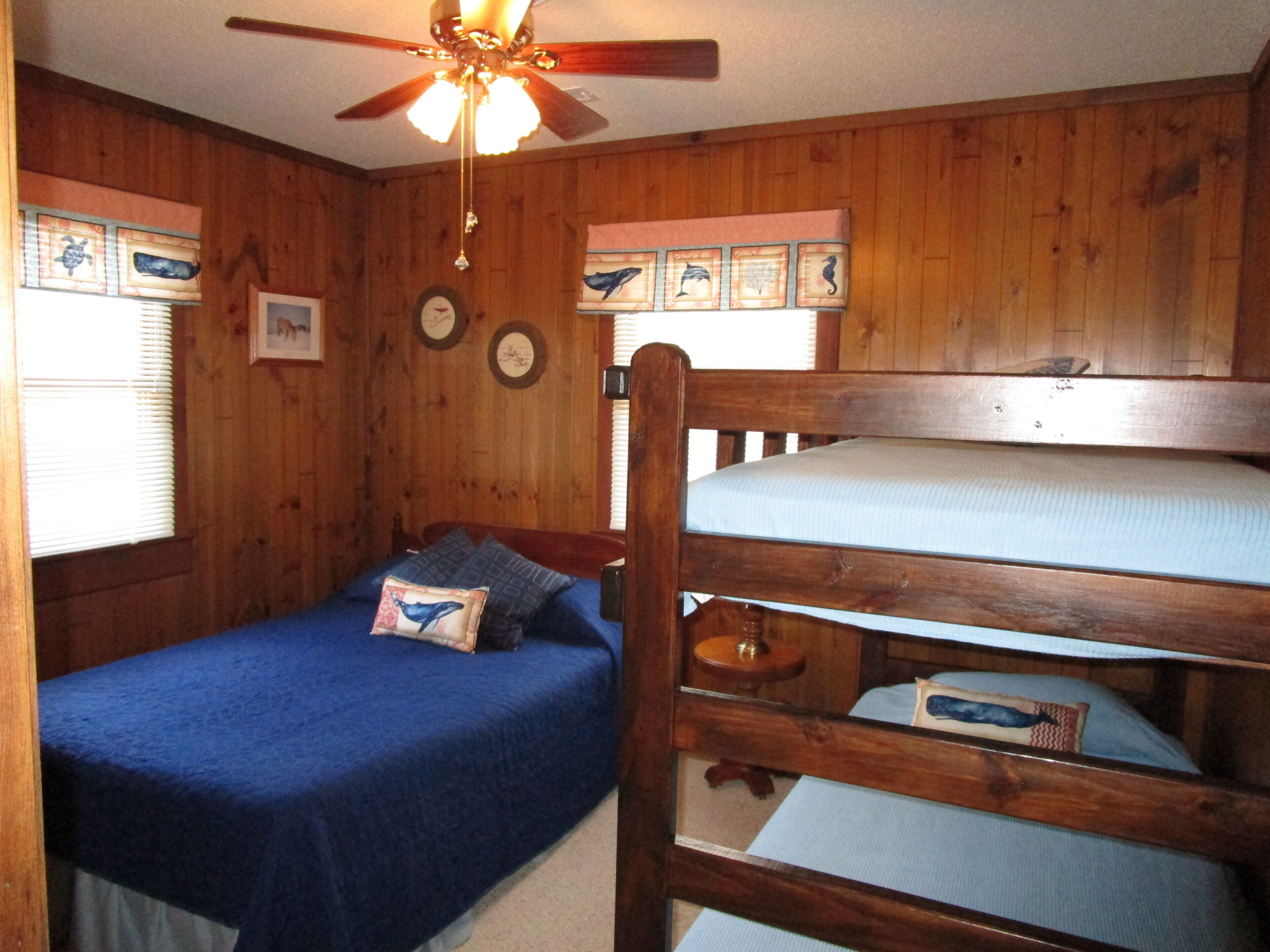 A cabin-style room with wooden walls, a bunk bed, a ceiling fan, and framed pictures on the wall.