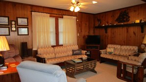 A cozy living room with wooden paneling, a ceiling fan, a television, and two sofas. - CAPTAINS QUARTERS - AN ALL INCLUSIVE VACATION RENTAL LOCATED IN SOUTHERN SHORES! (Kitty Hawk)