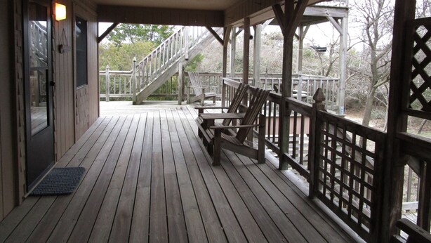 A wooden deck with a staircase leading to a higher level, a bench, and a door. - CAPTAINS QUARTERS - AN ALL INCLUSIVE VACATION RENTAL LOCATED IN SOUTHERN SHORES! (Kitty Hawk)