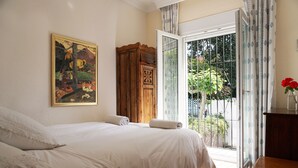 Une chambre à coucher avec un lit, une armoire en bois, un tableau accroché au mur et une vue sur l’extérieur, visible à travers une porte vitrée.