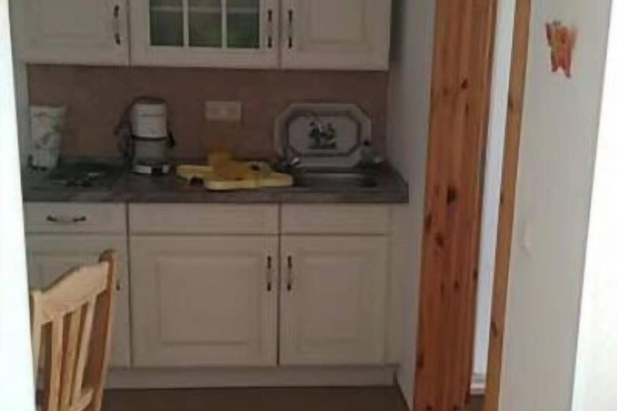 A compact kitchen with white cabinets, a wooden chair, and a tiled floor.