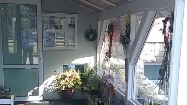 Un espace extérieur abrité, doté d’un banc en bois, de plantes en pot et d’une étagère murale où sont exposés divers objets.