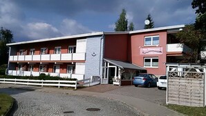 Un immeuble de deux étages avec une façade rouge et un balcon blanc. On peut y lire une enseigne indiquant « Hôtel-Restaurant ».