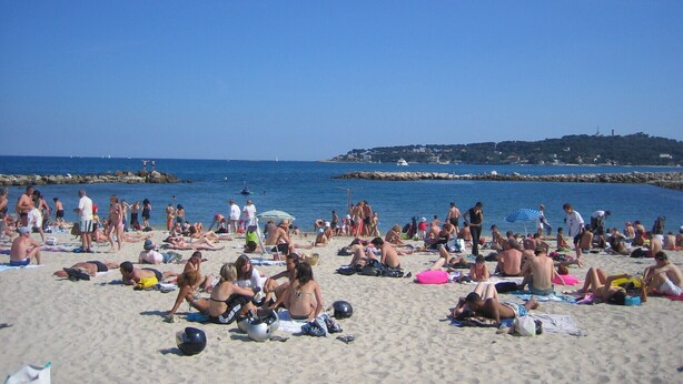 A crowded beach with people sunbathing and swimming.