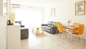 A modern living room with a grey sofa, a dining table with orange chairs, and a small coffee table.