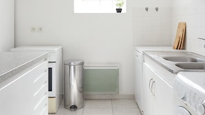 A modern kitchen with white cabinetry, a built-in oven, a stainless steel trash can, a radiator, and a washing machine.